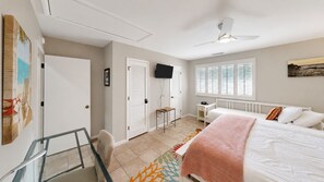 A bedroom with a bed, a TV, a desk, and a window with blinds. - Award-Winning Resort Amenities | Mariners Walk 9E (Isle Of Palms)