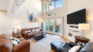 A spacious living room with a brown leather sofa, a coffee table, and a television. - Award-Winning Resort Amenities | Mariners Walk 9E (Isle Of Palms)
