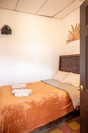 Ein Schlafzimmer mit einem Bett, Kissen, einem Wandventilator und einem dekorativen, sonnenähnlichen Objekt.