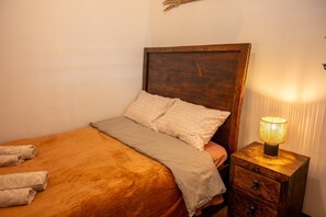 A bed with a wooden headboard, a bedside lamp, and a small wooden nightstand with drawers. - 360° Volcano View Apartment - Central Antigua (Antigua Guatemala)