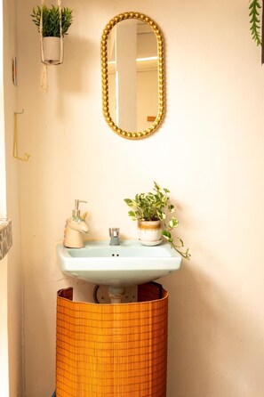 A bathroom with a light blue sink, a gold-framed mirror, a unicorn-shaped soap dispenser, and a potted plant with variegated leaves. - 360° Volcano View Apartment - Central Antigua (Antigua Guatemala)