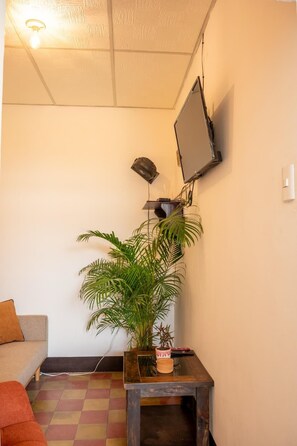 A room with a television mounted on the wall, a small table with a plant, and a checkered floor. - 360° Volcano View Apartment - Central Antigua (Antigua Guatemala)