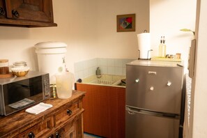 Eine Küche mit Mikrowelle, Kühlschrank, Holzschrank, Spüle und einer gefliesten Spritzschutzwand.