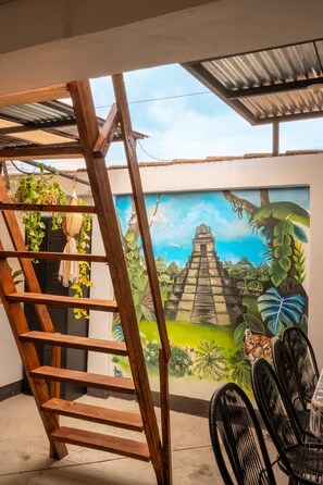 A wooden ladder, a mural of a pyramid, and black chairs in a room with a concrete floor. - 360° Volcano View Apartment - Central Antigua (Antigua Guatemala)