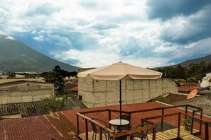 A rooftop terrace with a table and chairs, a beige umbrella, and a view of a mountain. - 360° Volcano View Apartment - Central Antigua (Antigua Guatemala)