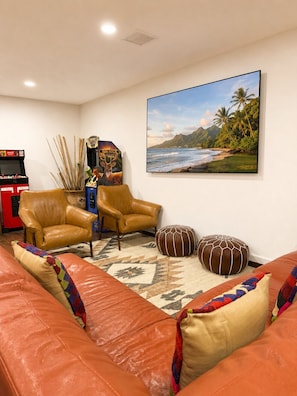A living room with a leather sofa, two armchairs, a coffee table, a wall-mounted TV, and a framed picture of a beach scene. - Rosolle Lux Ranch: H Pool, Hot Tub, Sauna, Outdoor Games & Game Room Relax Time (West Palm Beach)