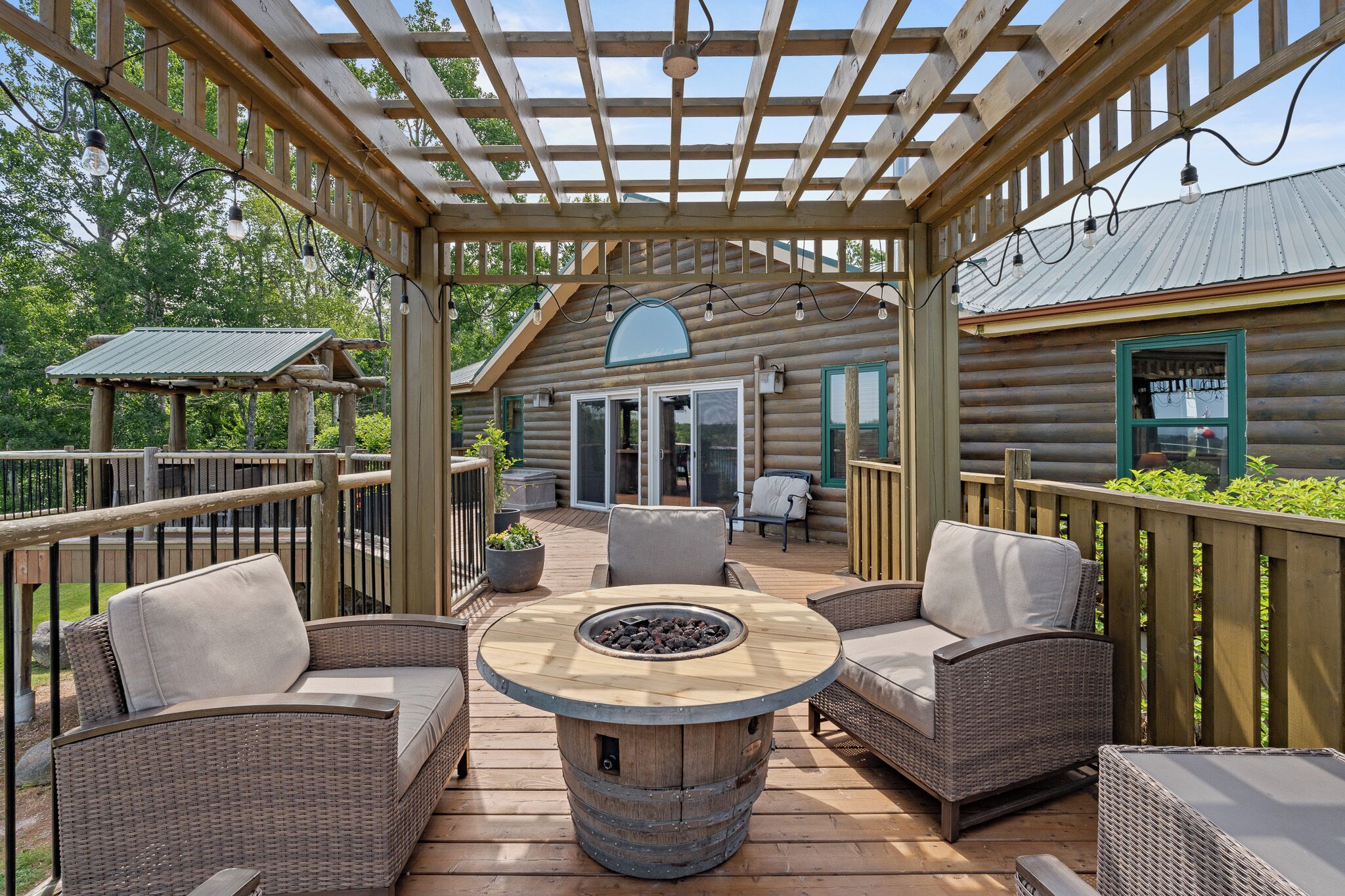 Une terrasse en bois avec des meubles en osier, un foyer et une structure en forme de pergola.