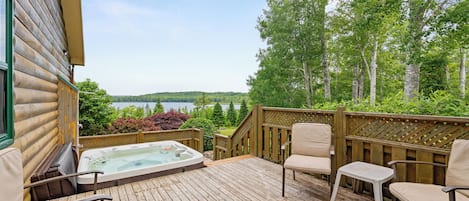 A wooden deck with a hot tub, chairs, and a view of a lake.