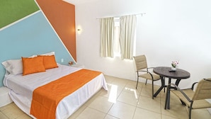 A hotel room with a bed, a table with chairs, a window with curtains, and a wall with a geometric design.