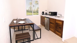 A compact kitchen with a dining table, bench, and a view of palm trees through a window.