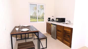 Cocina compacta con mesa de comedor, banco y vista a palmeras a través de una ventana.