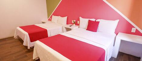 Habitación de hotel con dos camas, cada una con una colcha rojo y blanco, una mesita de noche con lámpara y un equipo de aire acondicionado instalado en la pared.