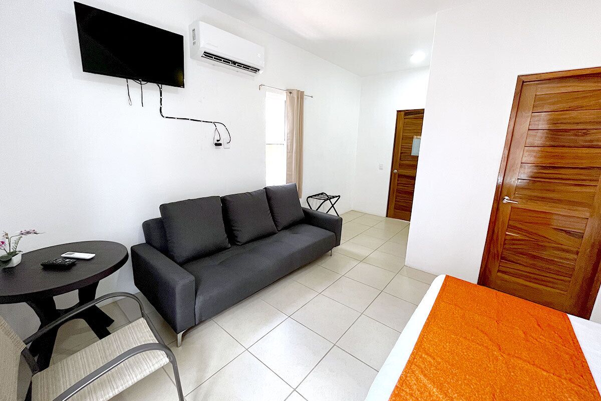 A room with a sofa, a small table, a TV mounted on the wall, and a door.