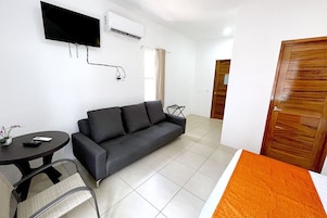 Une pièce comprenant un canapé, une petite table, un téléviseur fixé au mur et une porte.