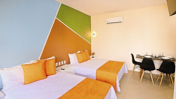 A hotel room with two beds, a dining table with chairs, and an air conditioning unit on the wall.
