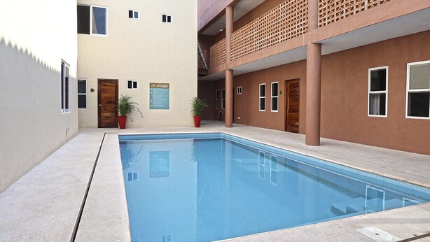 A swimming pool with a concrete deck, surrounded by buildings with multiple doors and windows.