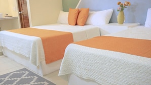 A hotel room with two beds, each with an orange blanket, white pillows, and a white quilted headboard. A vase with flowers is on the nightstand.