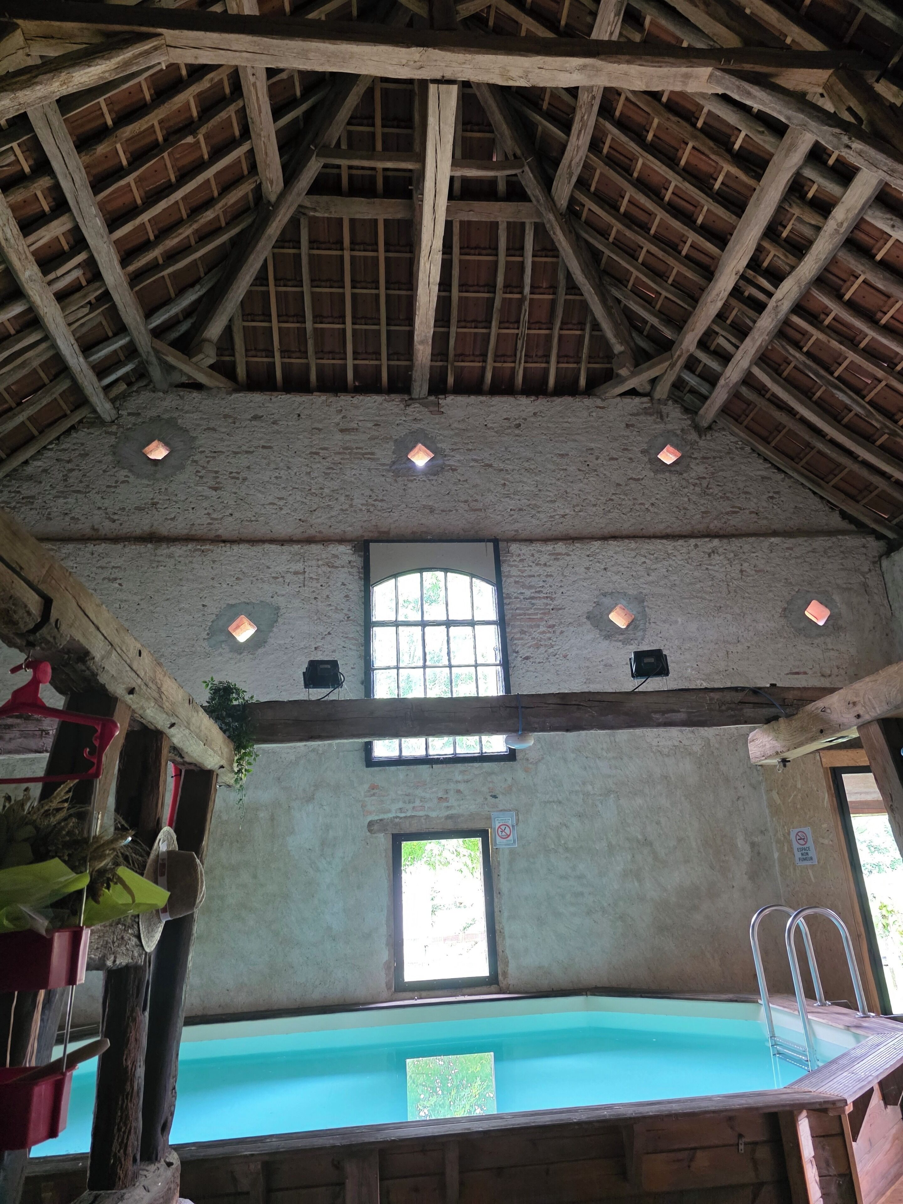 Ein rustikales Interieur mit Holzbalkendecke, Schwimmbecken und Fenster.