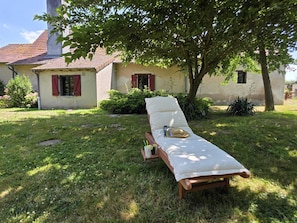 A sunlit outdoor lounge area with a wooden bench, a cushion, and a tray with a book and drinks. - Charming home, relaxation area, pets, nature, tranquility, activities (CHEZY)