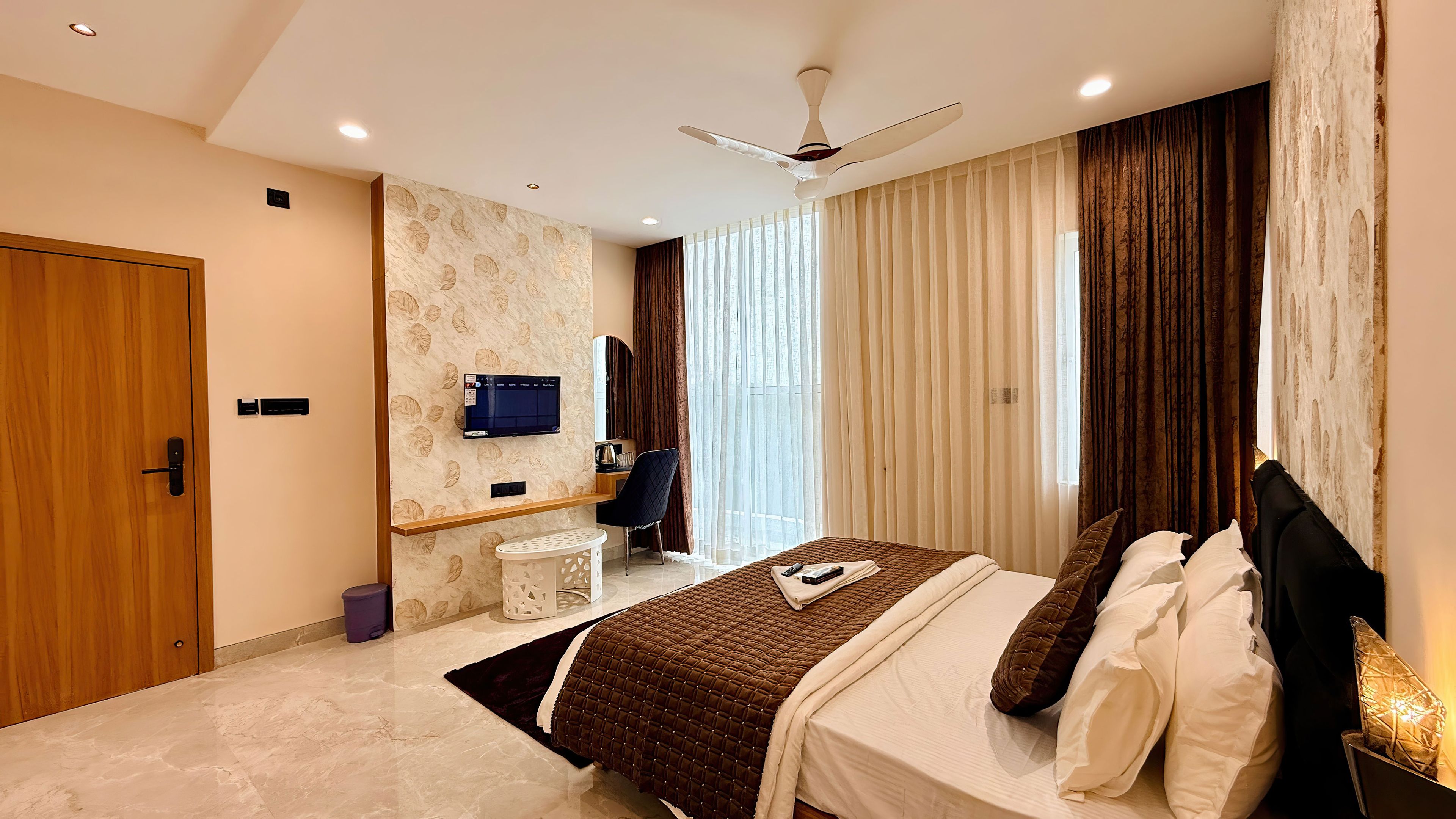 Une chambre d’hôtel équipée d’un lit, d’un bureau, d’une chaise, d’une télévision et d’un ventilateur de plafond.