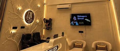 A hotel lobby with a lotus-themed ceiling, a reception desk, two armchairs, and a television screen.