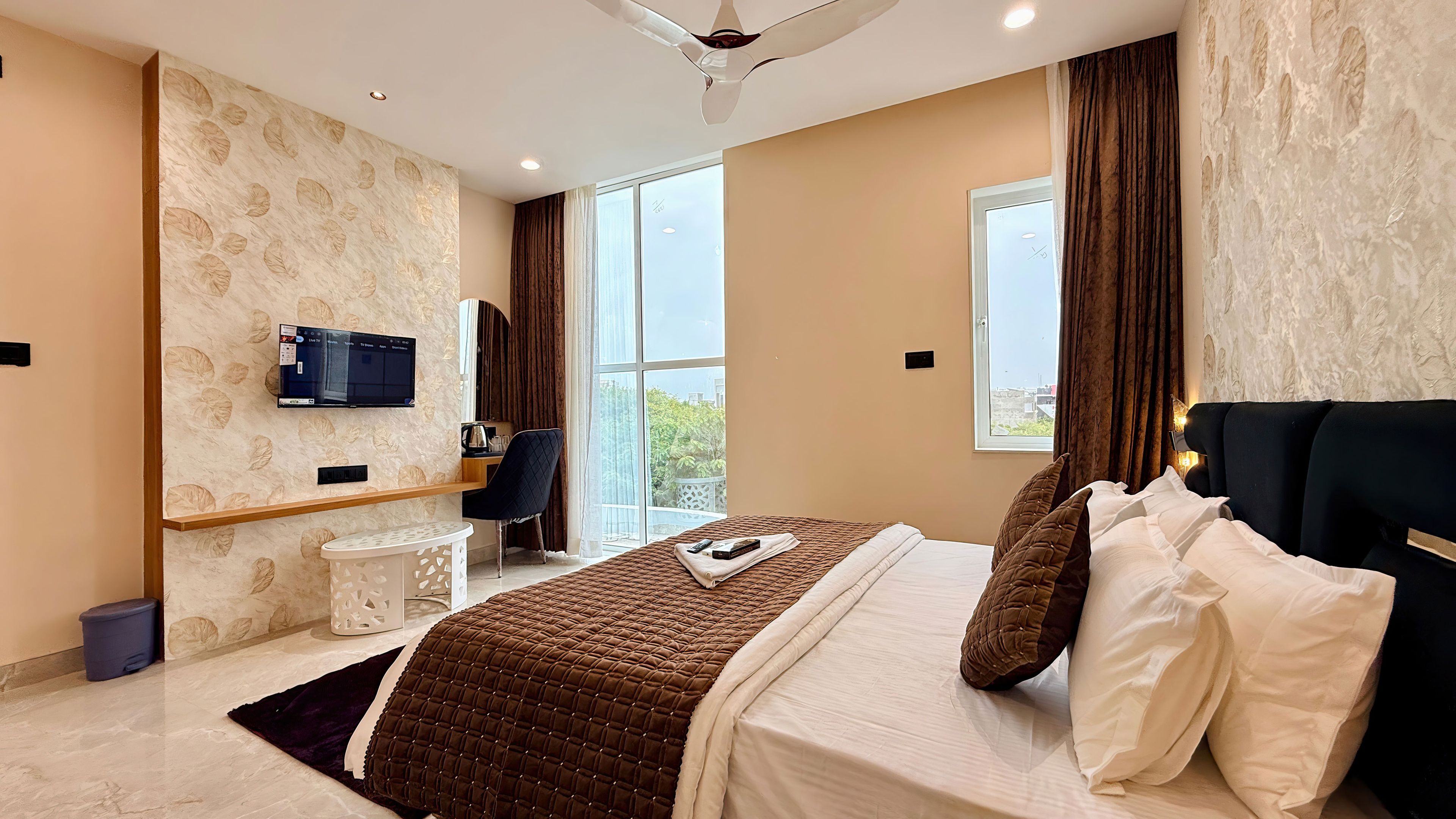 A modern hotel room with a bed, a desk, a TV, and a large window.