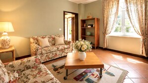 A living room with a sofa, a coffee table, a lamp, a bookshelf, and a window with curtains. - Gaetano Spadaro Estate, Frantoio Apartment on the Po River (Capannori)