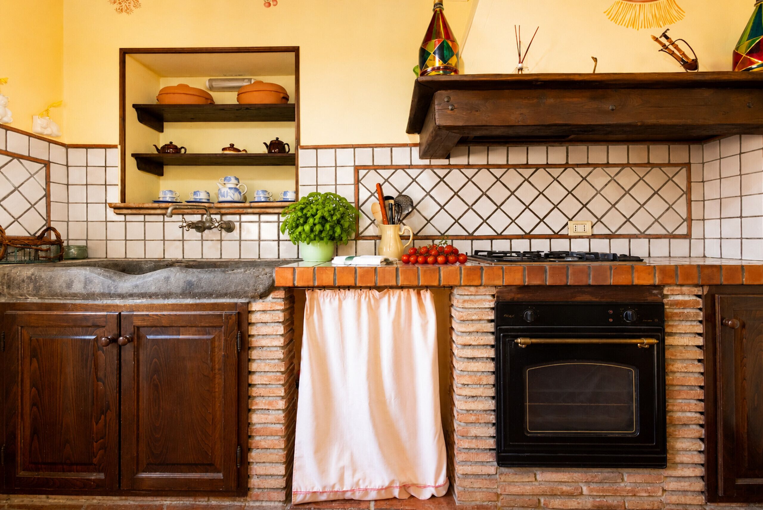 A kitchen with a brick backsplash, a gas stove, an oven, and a hanging shelf with kitchenware.