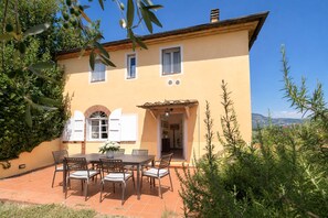 A two-story building with a patio area featuring a table and chairs, surrounded by greenery. - Gaetano Spadaro Estate, Frantoio Apartment on the Po River (Capannori)