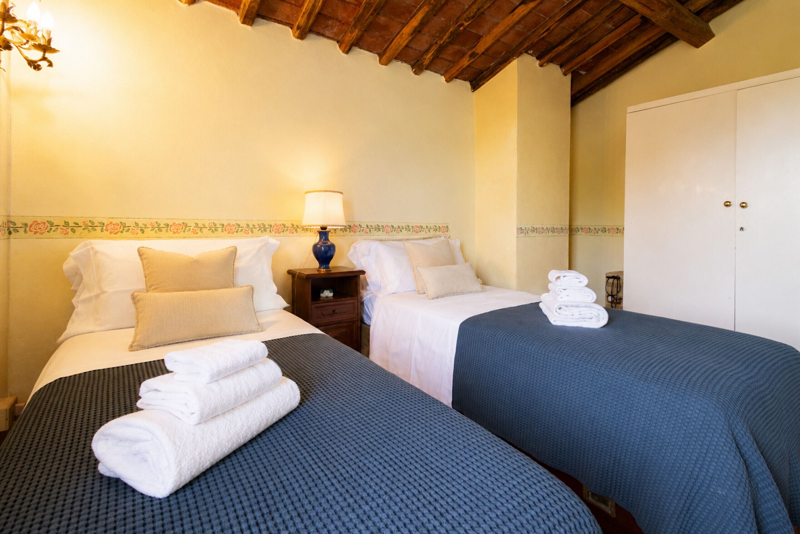 A hotel room with two beds, a nightstand with a lamp, and a wardrobe.