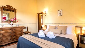 A hotel room with a large bed, a dresser, a mirror, and a vase with flowers. - Gaetano Spadaro Estate, Frantoio Apartment on the Po River (Capannori)