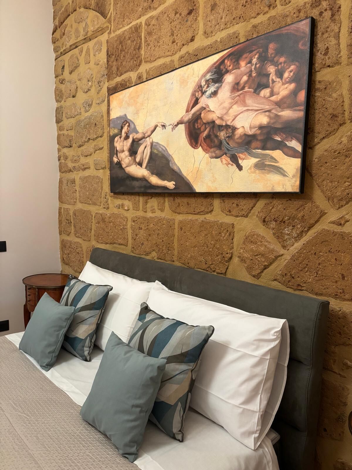 Un dormitorio con pared de piedra, una cama con almohadas y un cuadro.