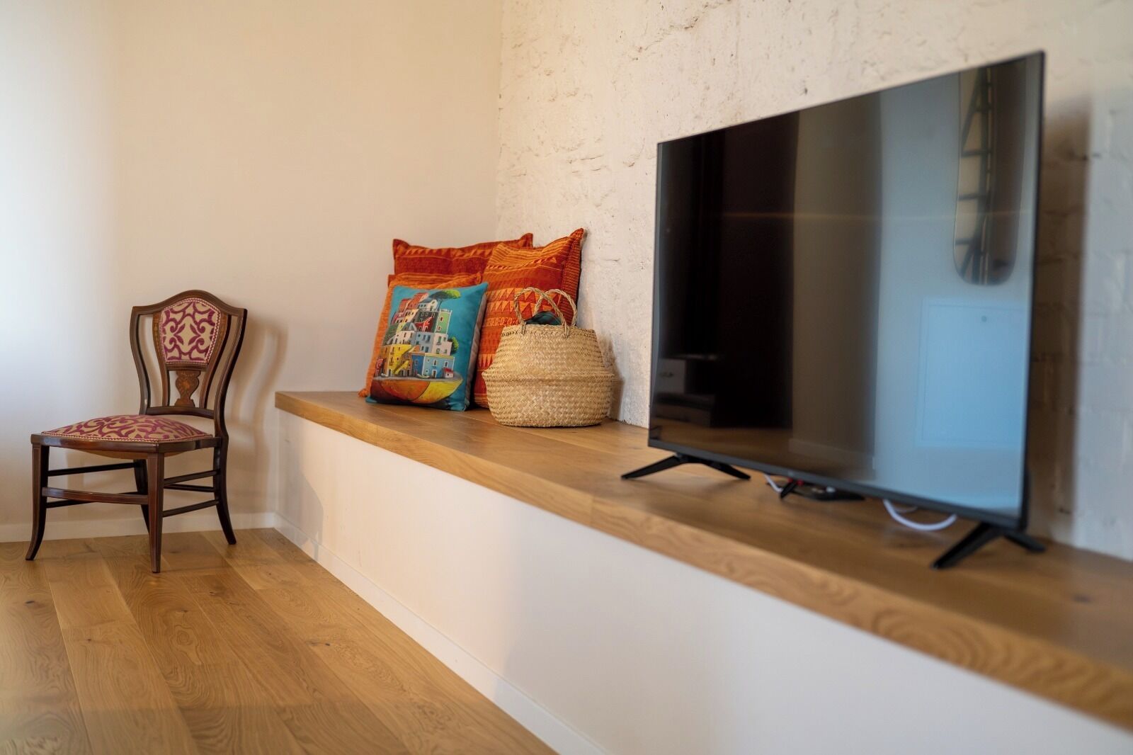 Una habitación con piso de madera, un banco de madera, un televisor y dos almohadones decorativos.