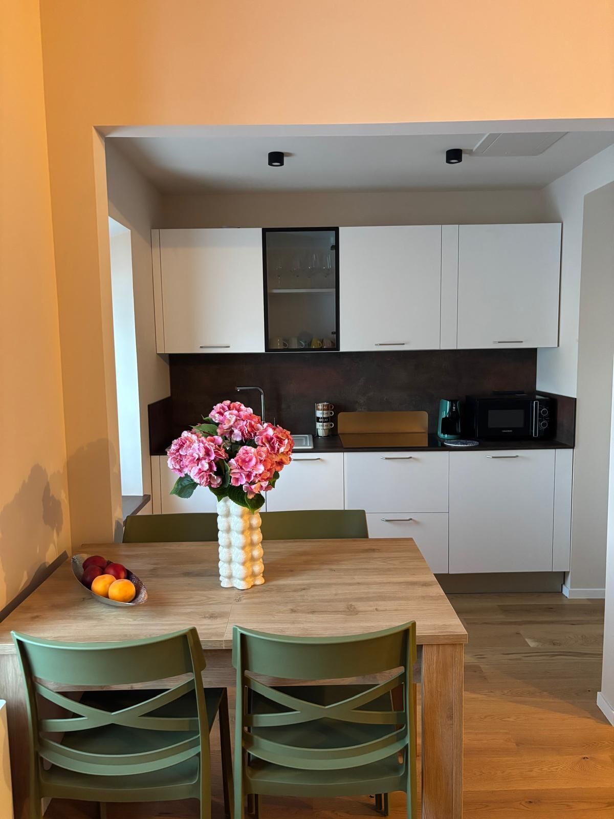 Un comedor con una mesa y sillas de madera, un florero y un frutero.