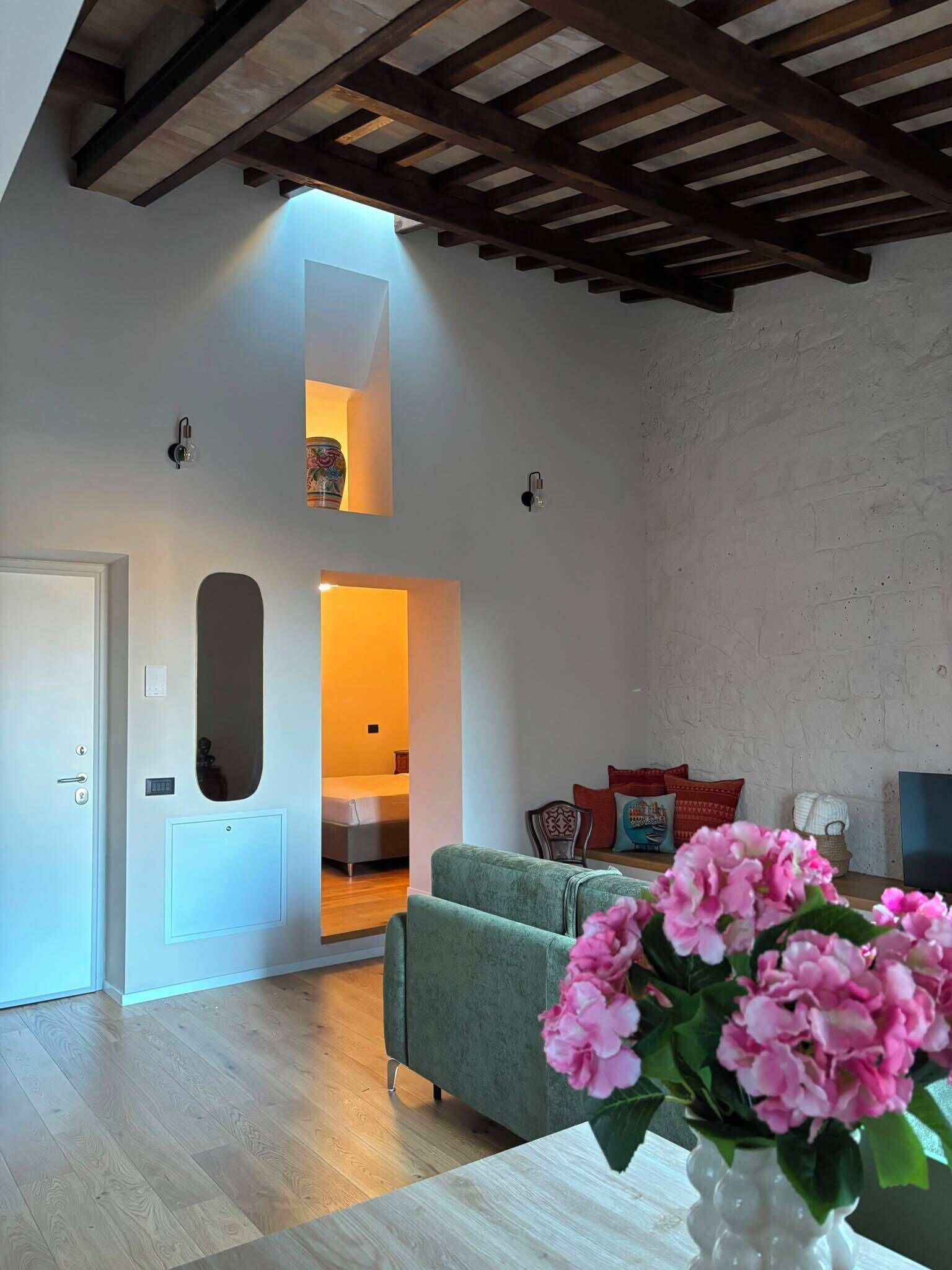 Een ruime woonkamer met een hoge plafond, een bank, een stoel en een vaas bloemen.