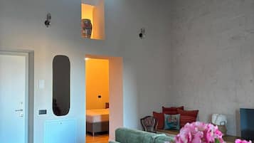 Een ruime woonkamer met een hoge plafond, een bank, een stoel en een vaas bloemen.