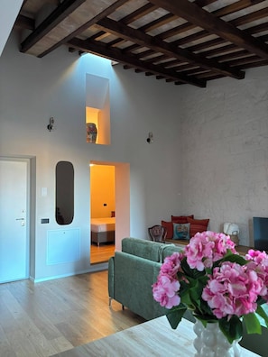 A spacious living area with a high ceiling, a sofa, a chair, and a vase of flowers. - Loggia Dei Mercanti 16 (Orvieto)