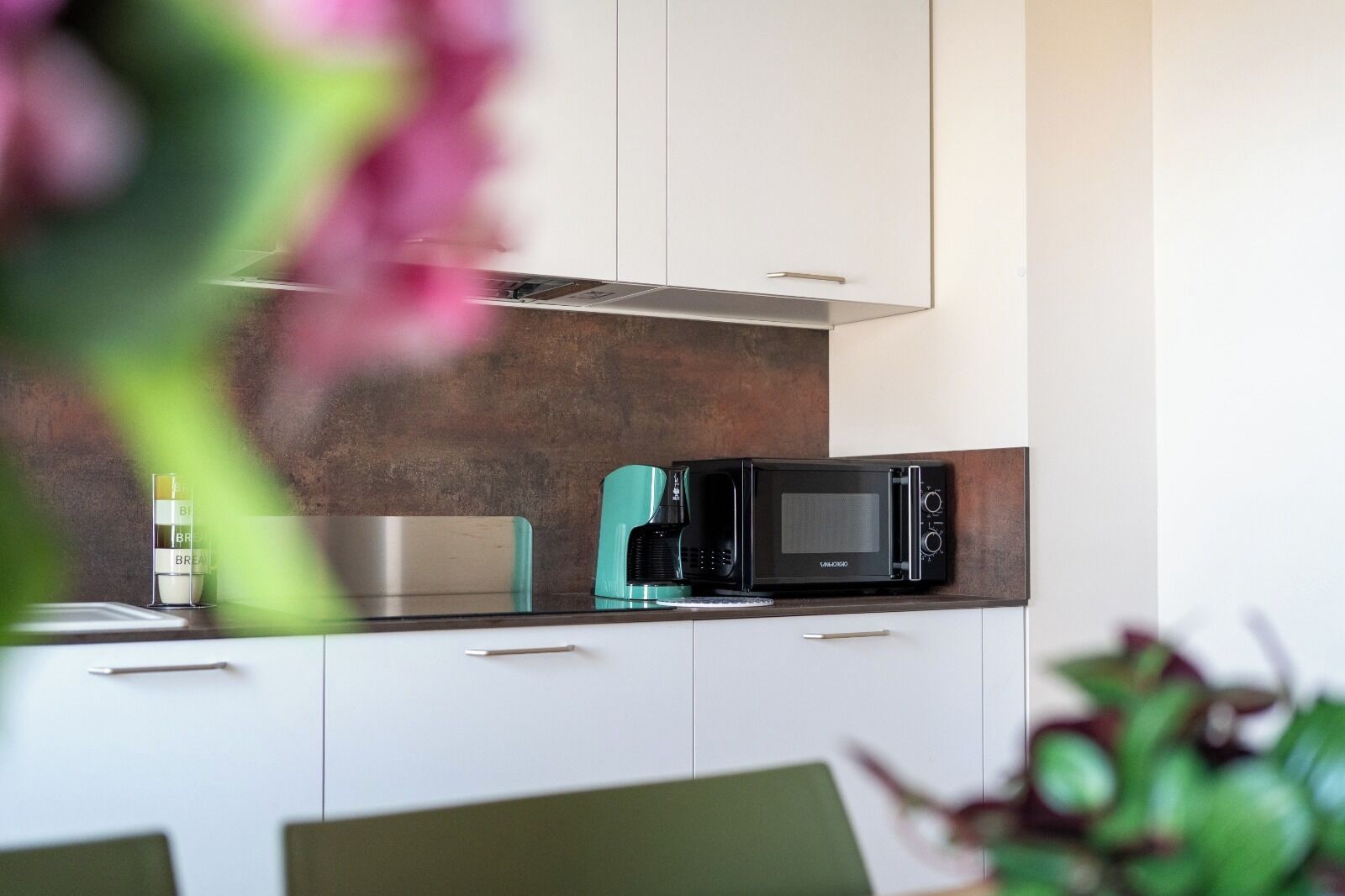 A modern kitchen with a built-in microwave, a coffee maker, and a scale on the countertop.