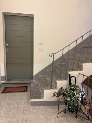 Eine Treppe mit Metallgeländer, eine graue Tür und ein kleiner Tisch mit Pflanzen.