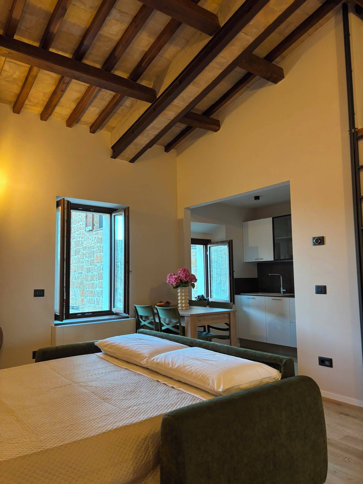 Un dormitorio con cama, escritorio y vista a la cocina por una puerta abierta.