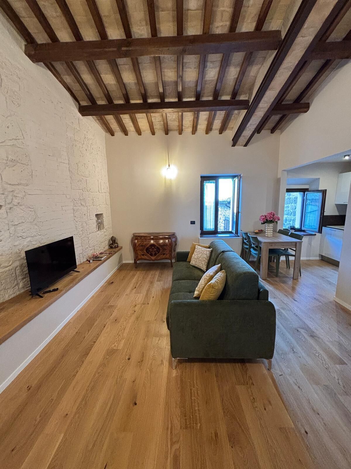 A living room with a wooden floor, a green sofa, a TV, and a dining area with a table and chairs.