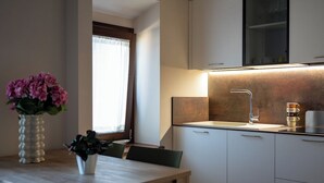 Moderni keittiö, jossa on valkoiset kaapit, ruostumattomasta teräksestä valmistettu pesuallas sekä puinen ruokapöytä tuoleineen.