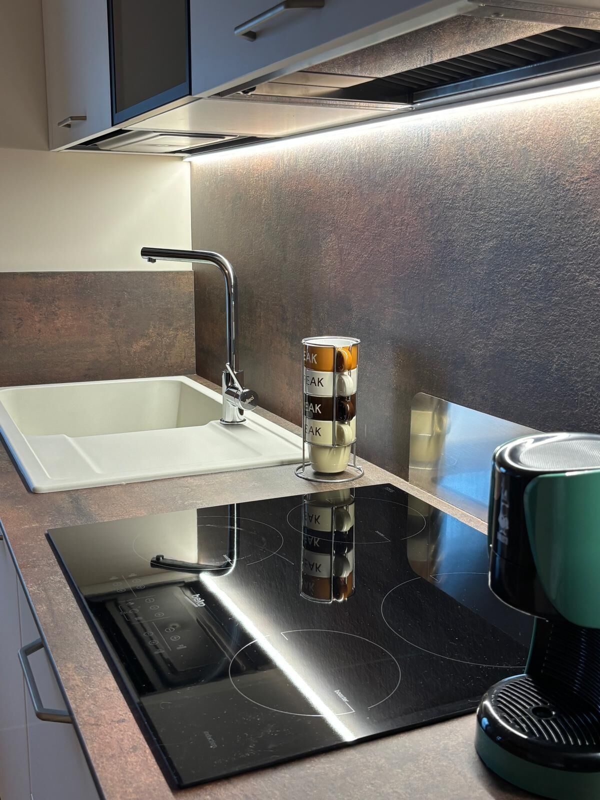 Ett modernt kök med en inbyggd spishäll, en diskho och en kaffebryggare.