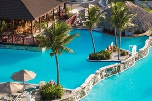 Poolbereich eines Resorts mit Palmen, Liegestühlen und einer Bar.