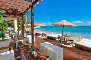 Eine HolzdTerrasse mit Sitzgelegenheiten und Sonnenschirmen mit Blick auf einen Strand.