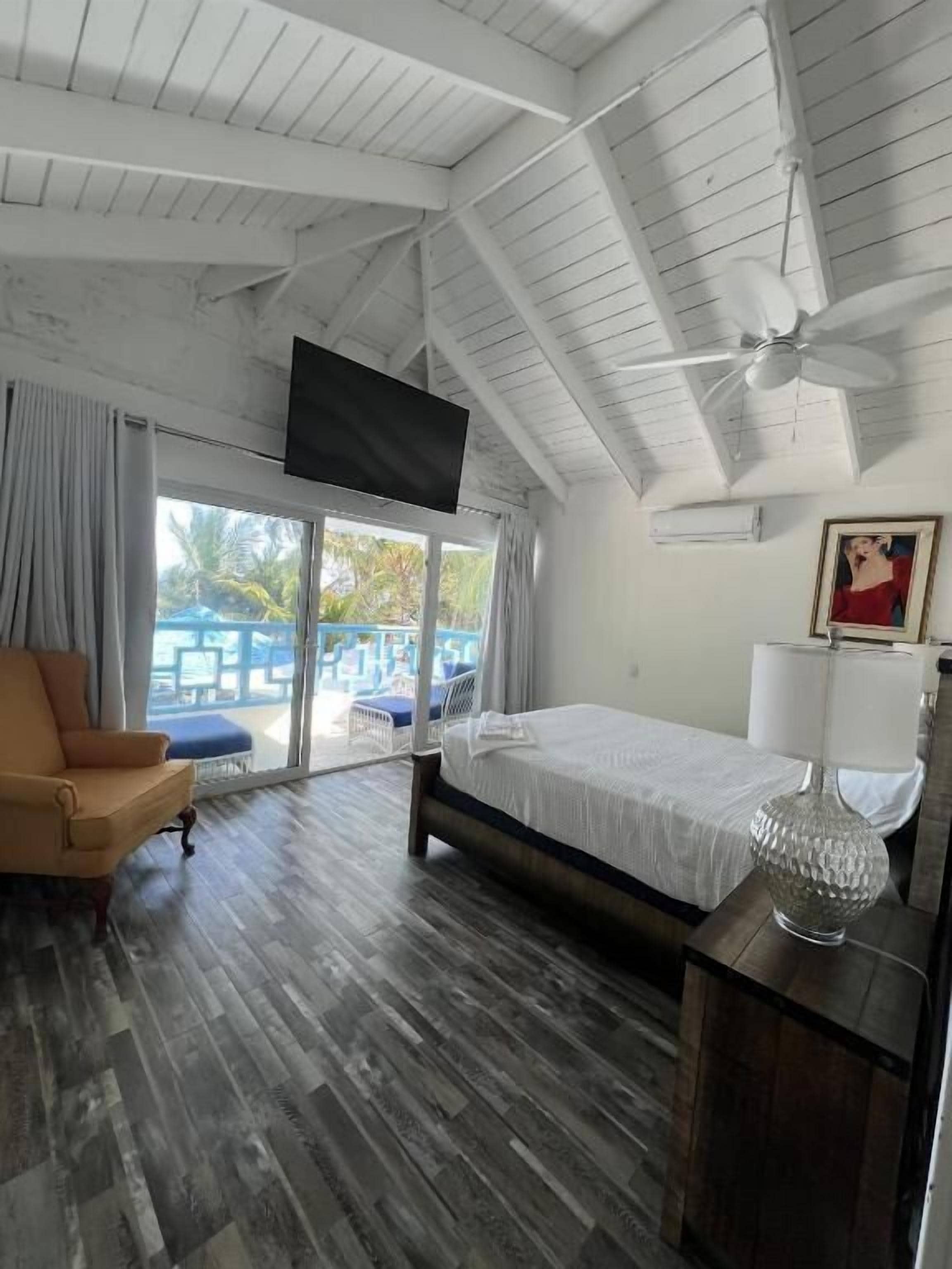 Un dormitorio con cama, una silla, televisor montado en el techo y vistas al exterior.