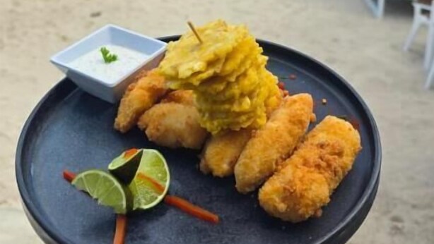 Un vassoio con cibo fritto e una fetta di lime su una spiaggia con palme e cielo sereno.