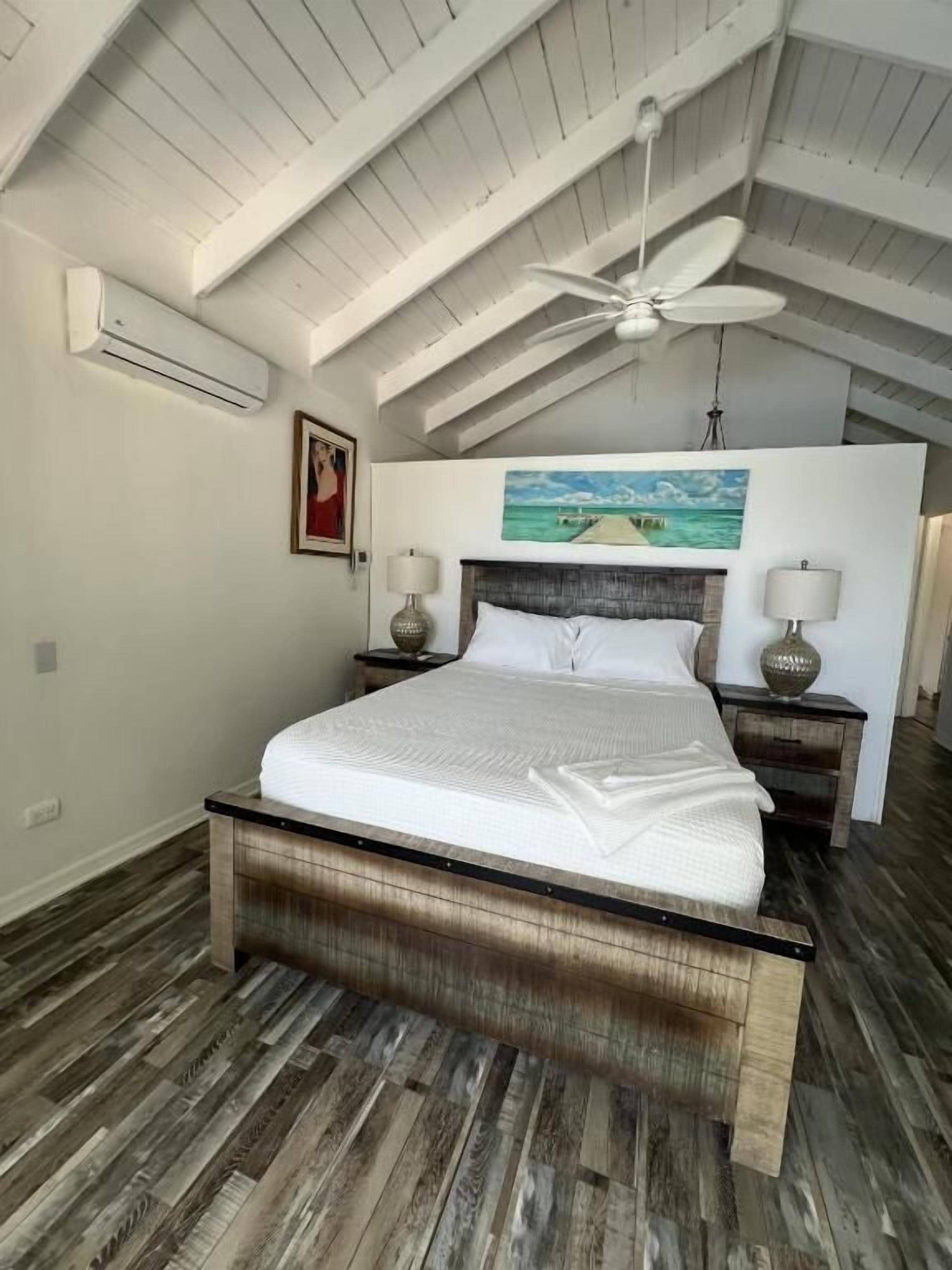 Un dormitorio con cama de madera, ventilador de techo y un cuadro en la pared.