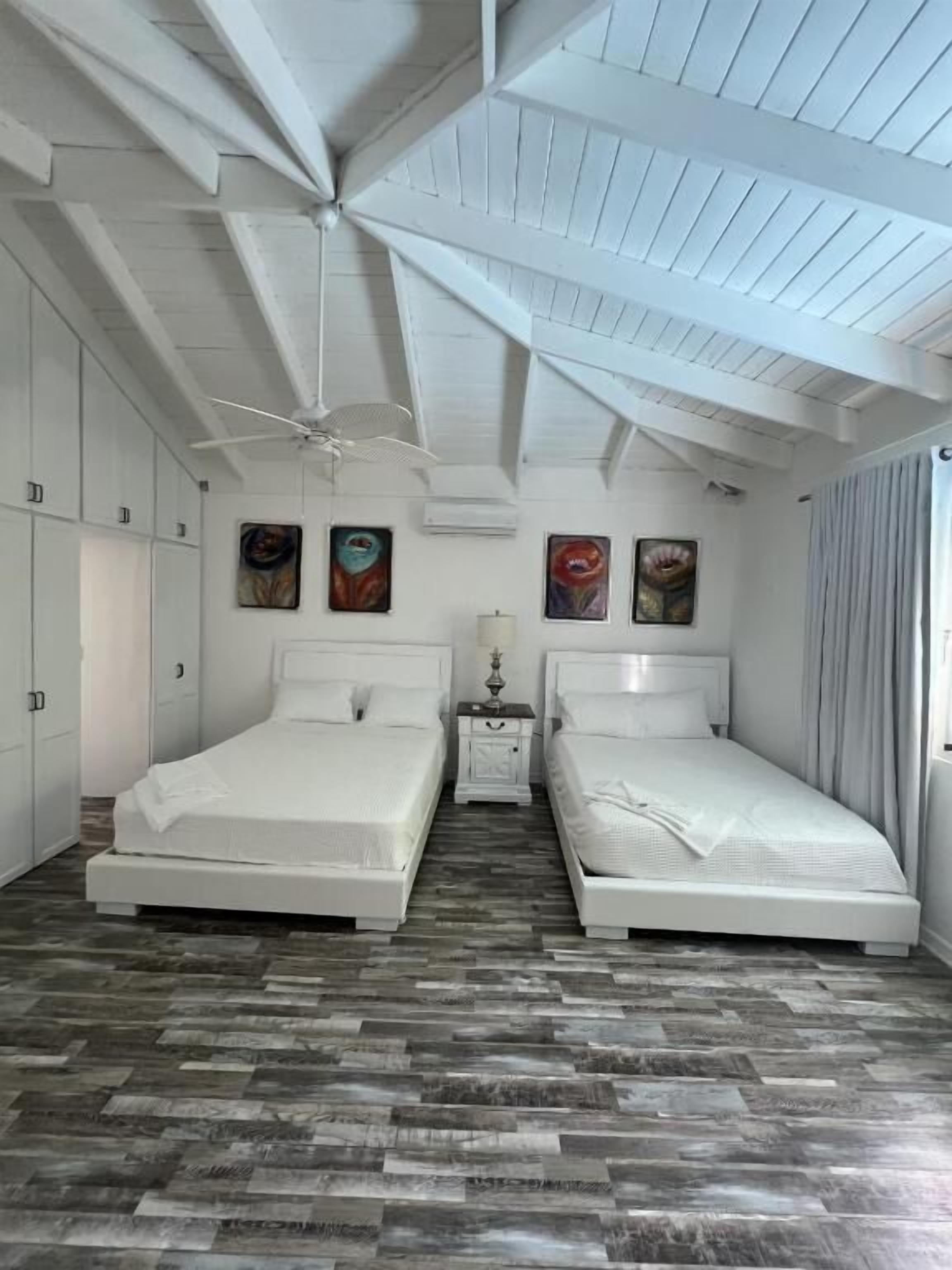 A bedroom with two beds, a ceiling fan, and artwork on the walls.