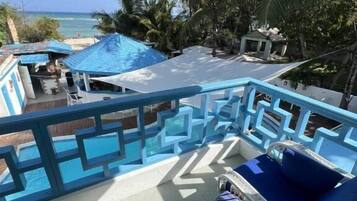 A balcony with a view of the ocean, a pool area, and a lounge chair.